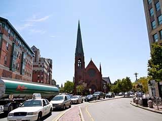 A photo of a brick church, with a line of cars in the foreground.