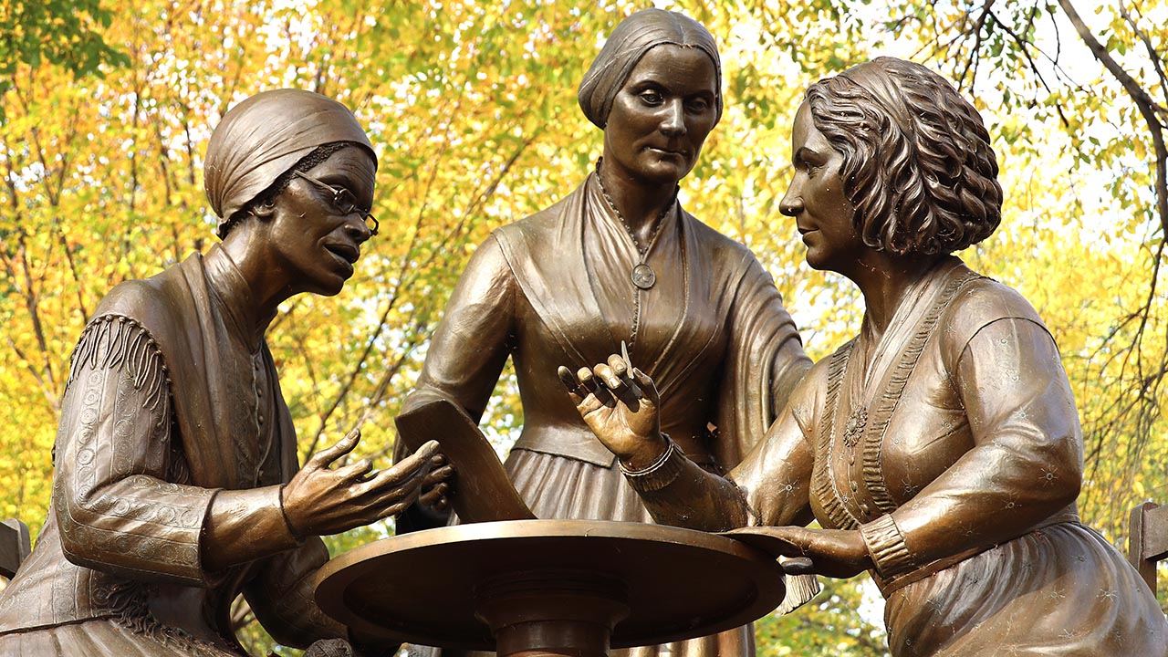 A bronze monument featuring three women gathered around a table.